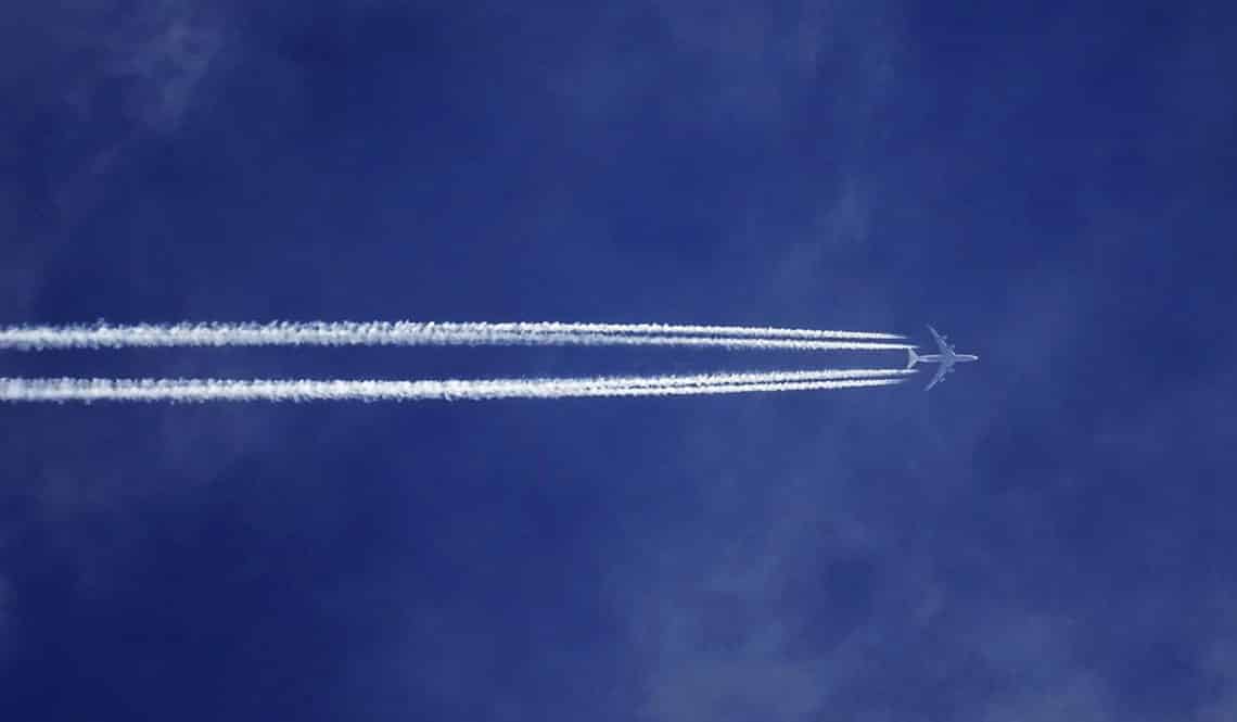 Auf dem Bild sind man ein Flugzeug am Himmel mit zwei Kondensstreifen. Der Himmel ist blau.